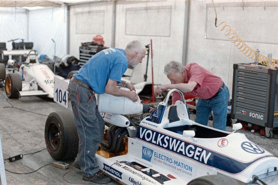 Two senior mechanics servicing race cars in a workshop garage.